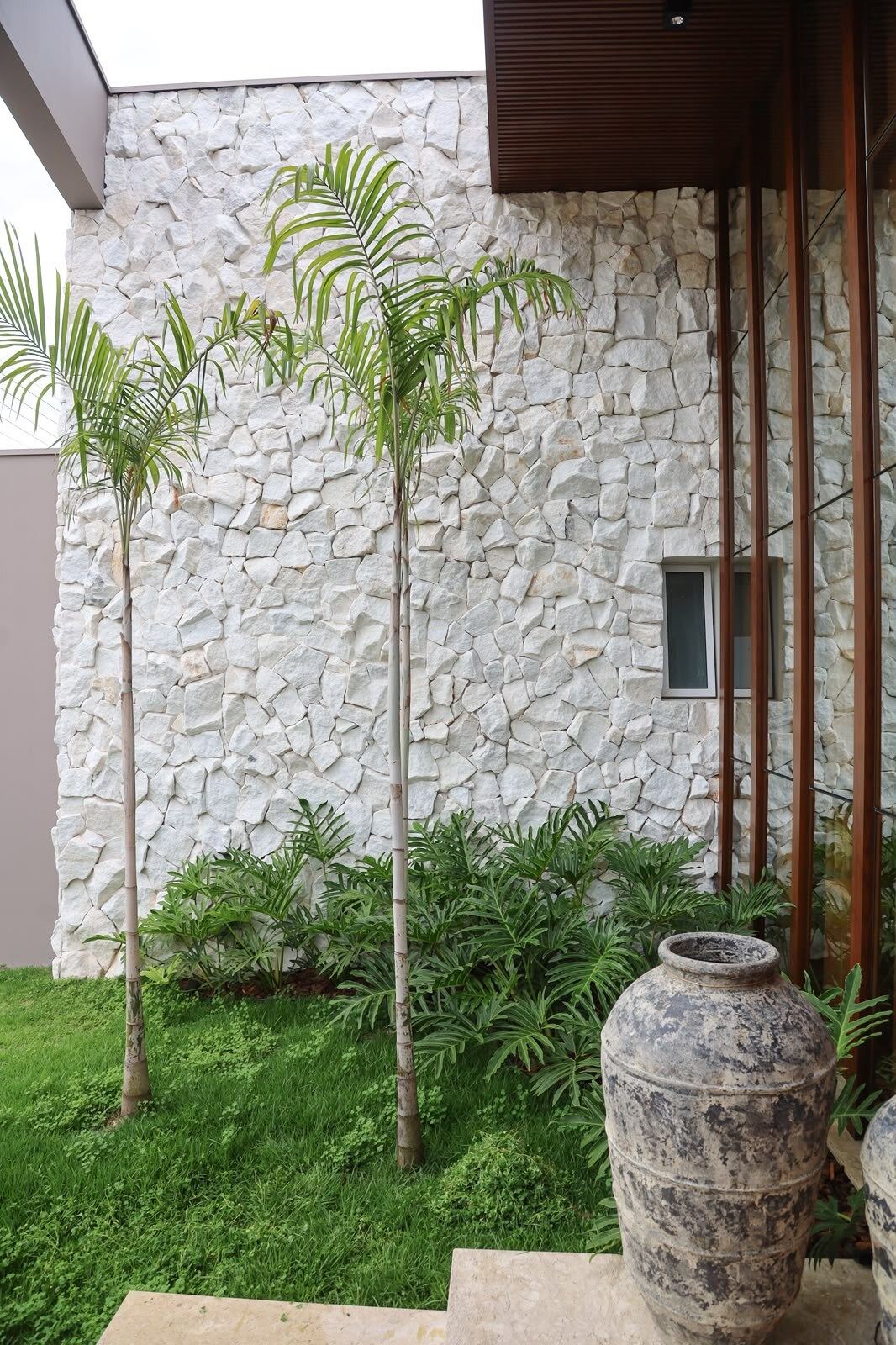 Fachada de residência com revestimento em pedra, palmeiras e vaso decorativo