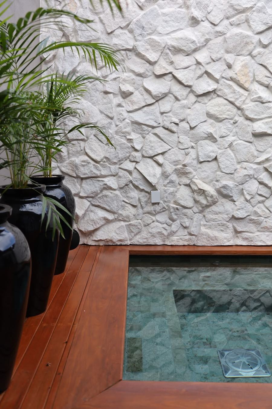 Parede de pedra ao lado de piscina com vasos pretos, opção de alto padrão
