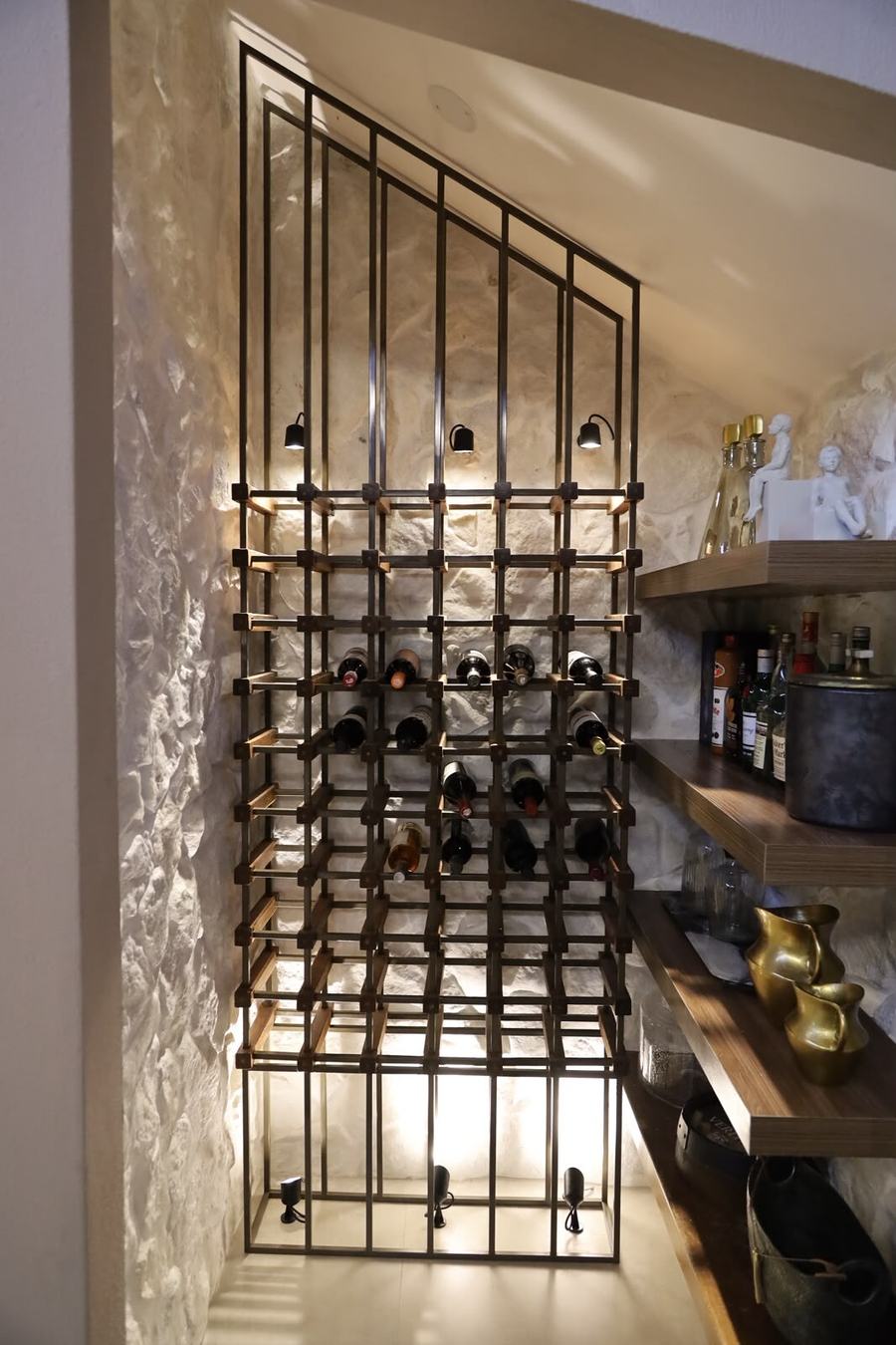 Adega decorativa com estrutura metálica junto à parede de pedra