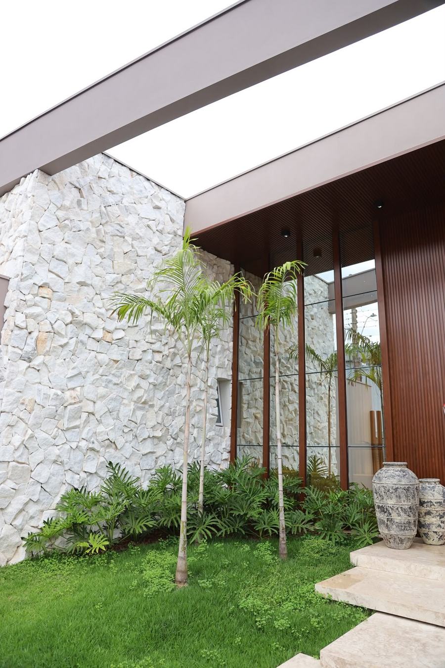 Fachada residencial em pedra com jardim e entrada em madeira